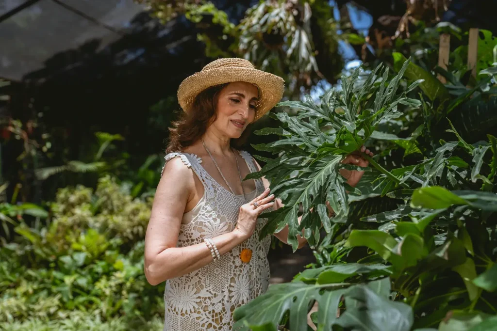 Femme avec un chapeau, une robe, les mains dans les plantes d'un jardin.