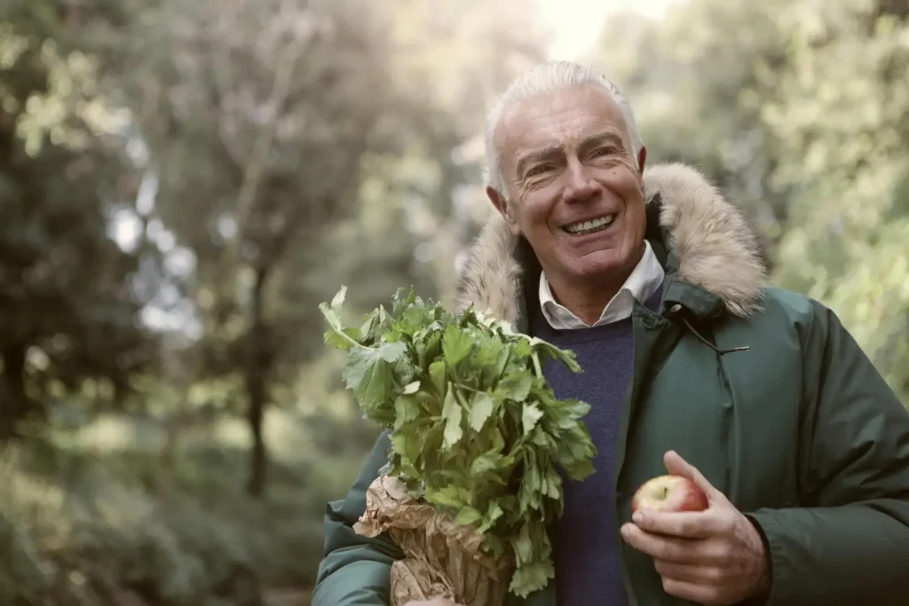 Un homme âgé avec une des légumes en mains et souriant.