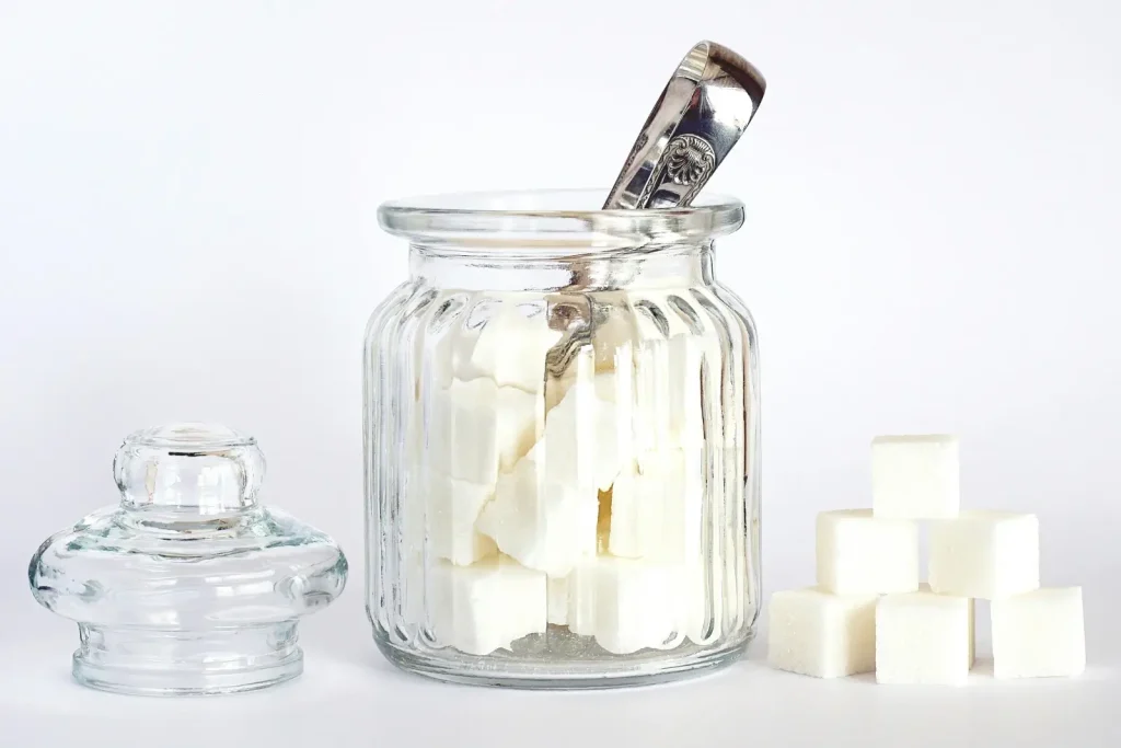 Bocal de sucre en verre avec pince en métal dedans.