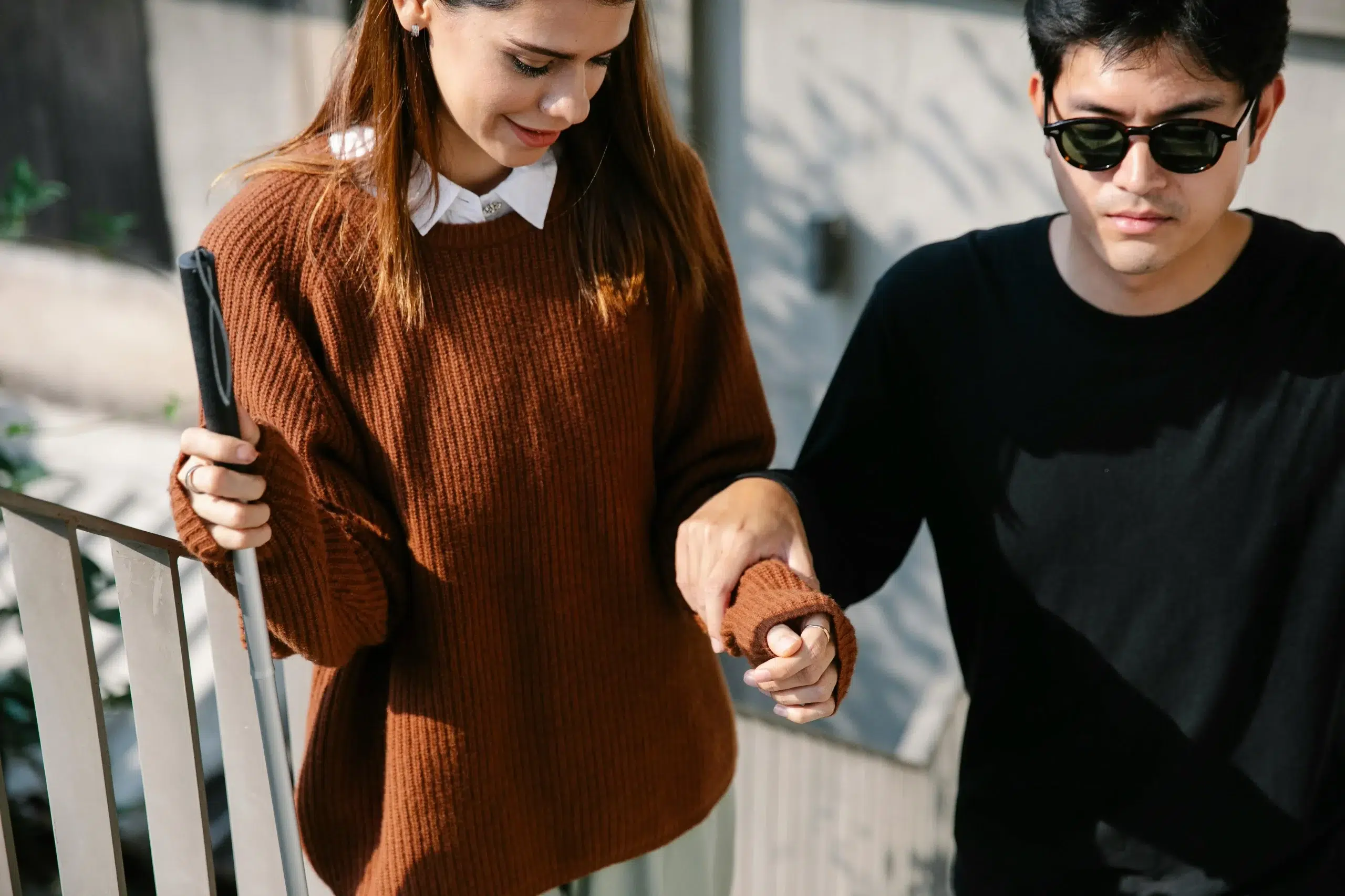 Deux personne se tenant la main. L'une porte des lunettes de soleils et atteint d'un handicap visuel.