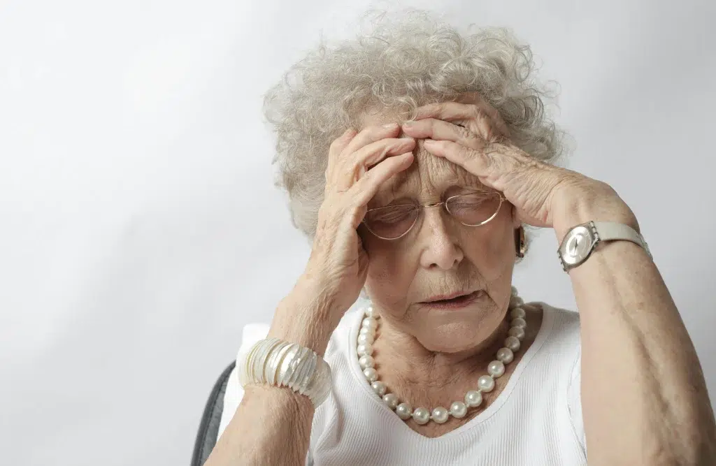 Femme âgée se tenant la tête à cause des symptômes physiques d'Alzheimer.